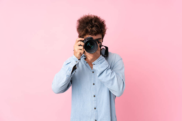 Fiatal fehér férfi izolált rózsaszín háttér egy professzionális kamera - Fotó, kép
