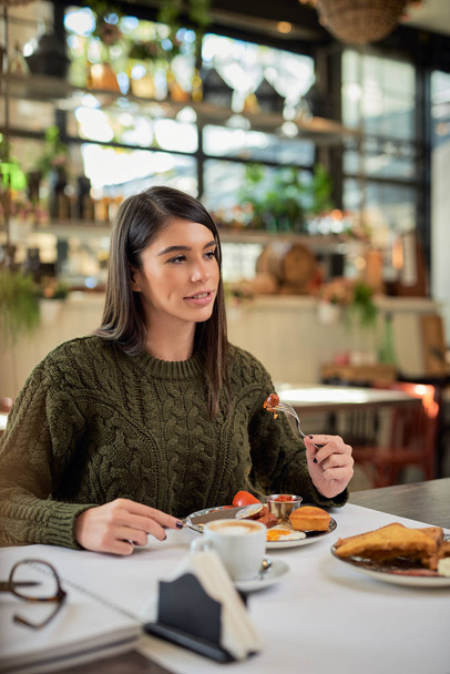 Attractive brunette sitting in restaurant in morning and eating breakfast. - Photo, Image