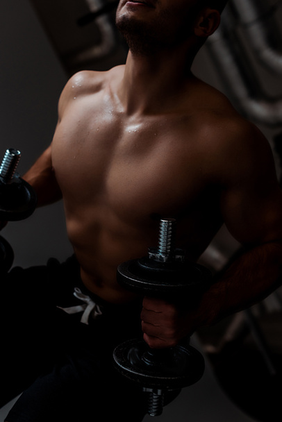 Ausgeschnittene Ansicht eines muskulösen Bodybuilders mit nacktem Oberkörper, der mit Hanteln trainiert - Foto, Bild