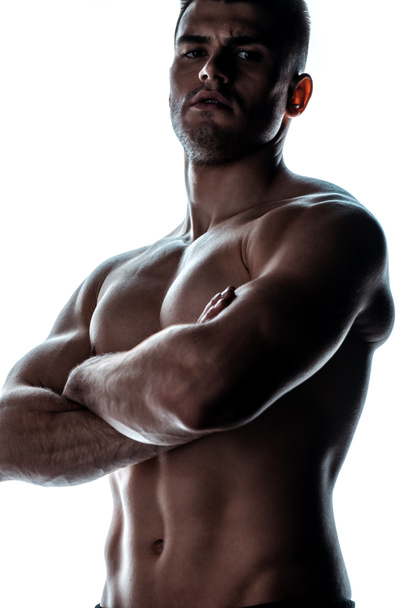 sexy muscular bodybuilder with bare torso posing with crossed arms in shadow isolated on white - Fotó, kép
