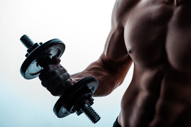 cropped view of sexy muscular bodybuilder with bare torso exercising with dumbbell on white - Photo, Image