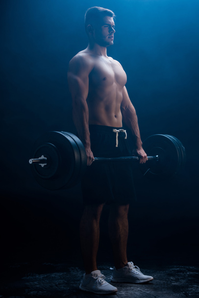 sexy muscular bodybuilder with bare torso excising with barbell on black background with smoke  - Φωτογραφία, εικόνα