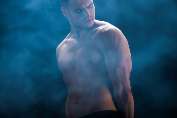 sexy muskulöser Bodybuilder mit nacktem Oberkörper auf schwarzem Hintergrund mit Rauch - Foto, Bild