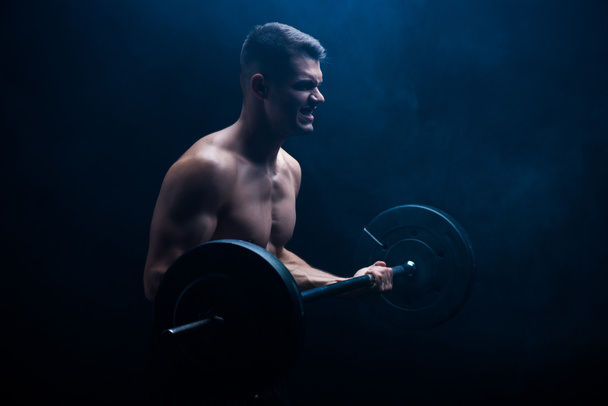 tense sexy muscular bodybuilder with bare torso excising with barbell on black background - Photo, Image