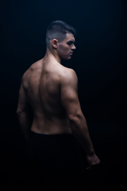 back view of sexy muscular bodybuilder with bare torso posing isolated on black - Photo, Image
