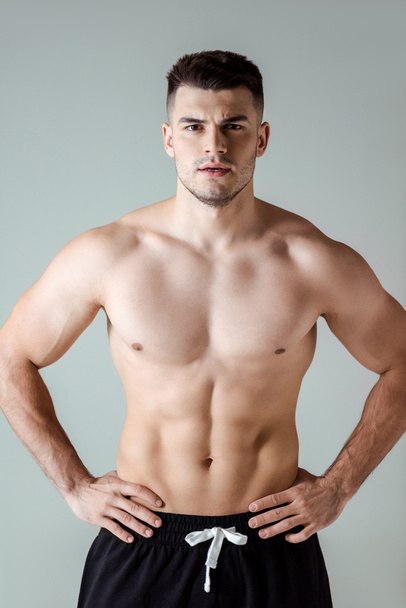 sexy muscular bodybuilder with bare torso posing with hands on hips isolated on grey - Fotó, kép