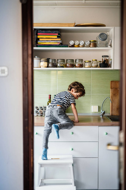 Kleiner Junge klettert auf Arbeitsplatte in seiner Küche - Foto, Bild