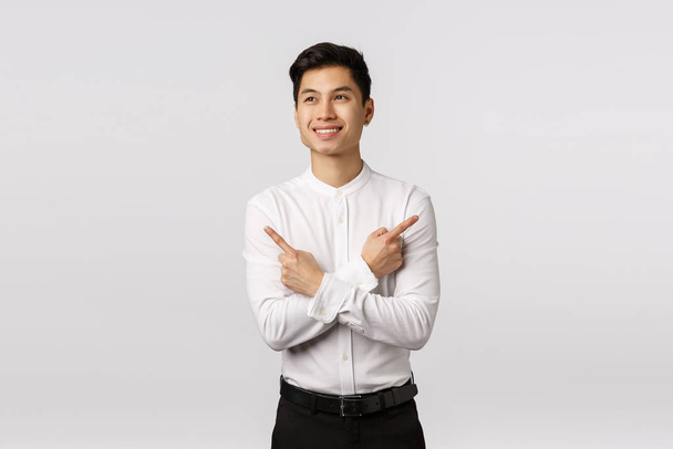 Marzycielski i szczęśliwy, optymistyczny azjatycki biznesmen wierzy w siebie, zaczyna nową pracę po ukończeniu studiów, wskazuje bokiem, dwa warianty pokazujące, spójrz w lewo, stojące białe tło - Zdjęcie, obraz