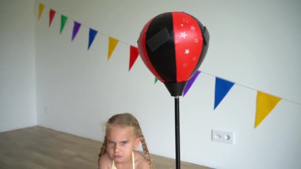Angry child girl sit near punching bag and boxing gloves. Camera moving down - Footage, Video
