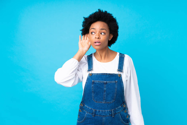 African american woman with overalls over isolated blue background listening something - Foto, immagini