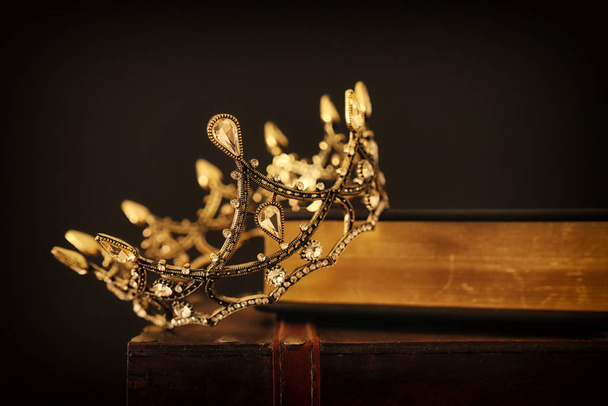 low key image of beautiful queen/king crown over old book and wooden table. vintage filtered. fantasy medieval period - Fotografie, Obrázek
