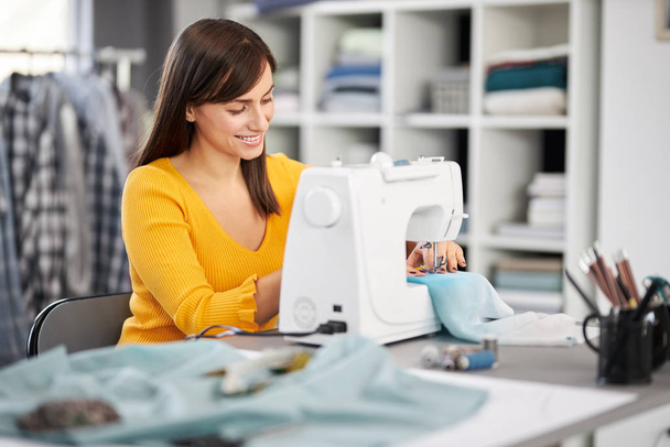 Smiling charming caucasian fashion designer sitting in her studio and sewing beautiful evening dress. - Φωτογραφία, εικόνα