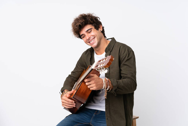 Junger kaukasischer Mann mit Gitarre vor isoliertem weißem Hintergrund lacht - Foto, Bild