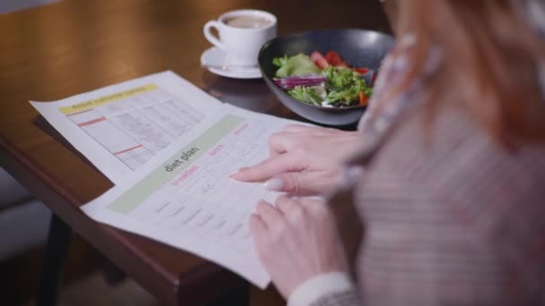 attractive young girl leads healthy lifestyle adheres to proper nutrition and checks the calorie content of products in diet plan while sitting at table in fashionable institution - Filmmaterial, Video