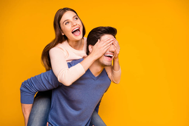 Positive cheerful woman close cover her spouse man eyes hug embrace piggy-back enjoy valentine day celebration wear blue pink sweater isolated over yellow color background - Fotoğraf, Görsel
