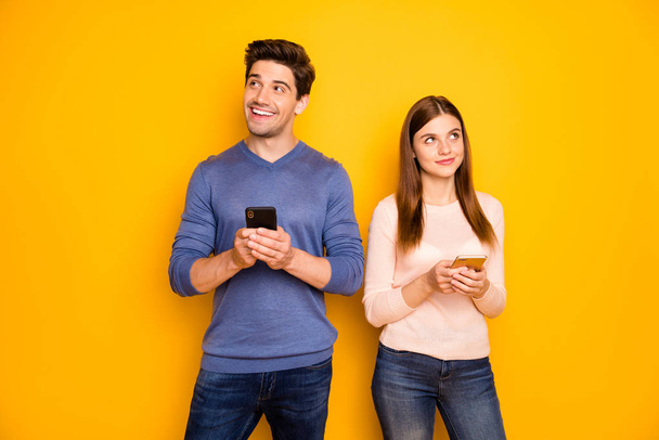 Portrait of inspired two students people married couple use smartphone think thoughts what post on social network wear blue pink pullover denim jeans isolated over yellow color background - Фото, изображение