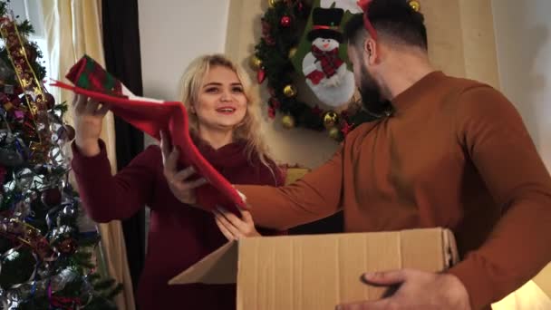 Portrait of cheerful Caucasian girlfriend and boyfriend choosing place for Christmas sock at home. Young man and woman decorating house on New Years eve. Holidays, celebration, preparations. - Filmmaterial, Video
