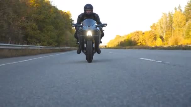 オートバイ愛好家は田舎道でバイクレースをしている。高速道路で現代のスポーツバイクに乗ってヘルメットで若い男。旅行中にバイクを運転する男。冒険の概念。フロントビューを閉じる - 映像、動画