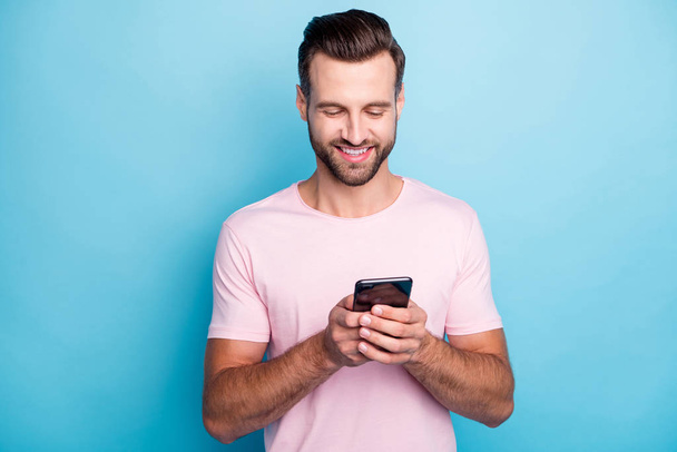 Closeup photo of attractive guy holding telephone hands blogger writing new comments modern technology person wear casual pink t-shirt isolated blue color background - Фото, зображення