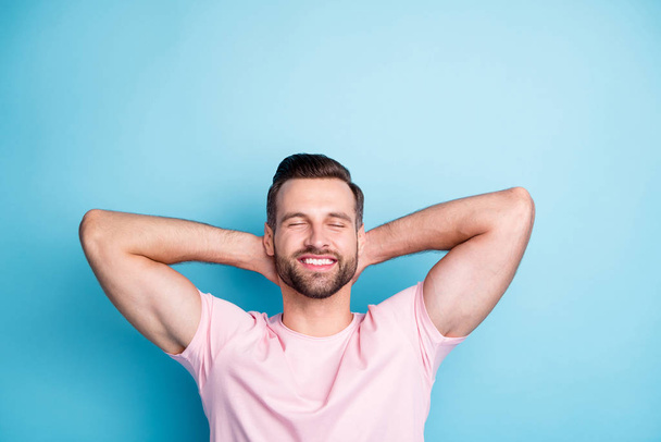 Photo of attractive guy holding hands behind head eyes closed enjoy amazing weekend day relaxing wear casual pink t-shirt isolated blue color background - 写真・画像