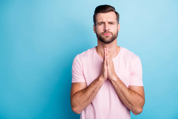 Please forgive me. Photo of attractive guy holding hands together asking girlfriend to forgive him did great mistake wear casual pink t-shirt isolated blue color background - Photo, Image