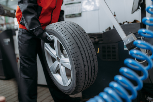Repairman puts the wheel on the balancing machine, tire service. Man repairs car tyre in garage, automobile on lift jack, inspection in workshop - 写真・画像