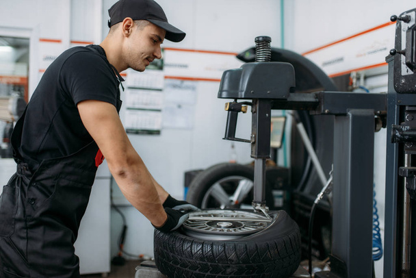 Mechanické upevnění rozbitého kola na montážní stroj, oprava. Muž opravuje pneumatiky v garáži, automobilová kontrola v dílně - Fotografie, Obrázek