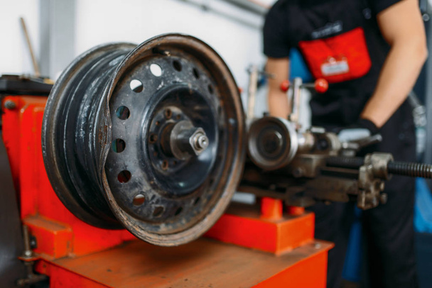 Repairman works with crumpled disc, tire repairing service. Man fixing car tyre in garage, professional automobile inspection in workshop - Photo, image