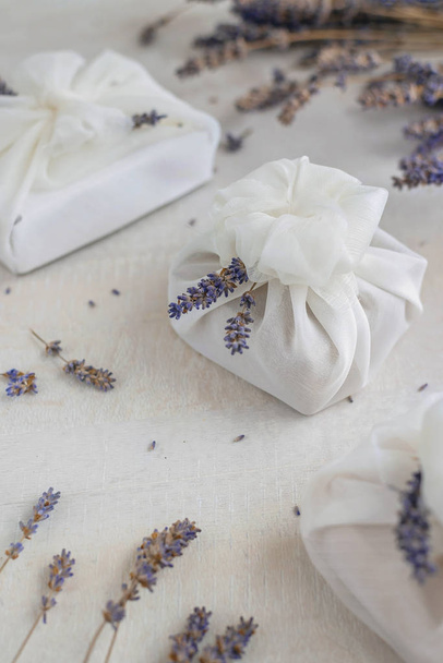 Presente envolto com tecido furoshiki branco e decorado com flores de lavanda. Eco presente amigável
. - Foto, Imagem