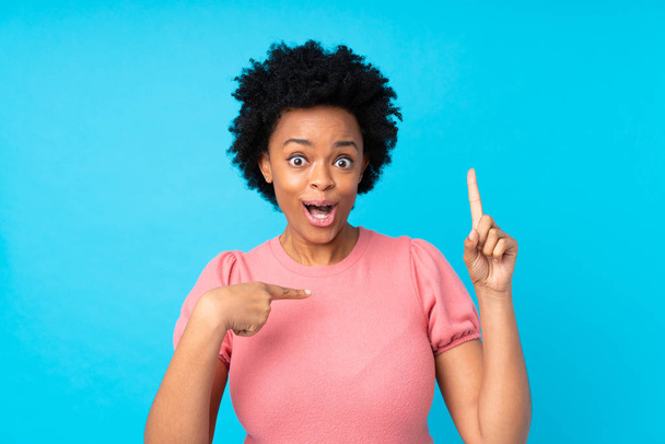 Afrikanische Amerikanerin über isoliertem blauen Hintergrund mit überraschendem Gesichtsausdruck - Foto, Bild