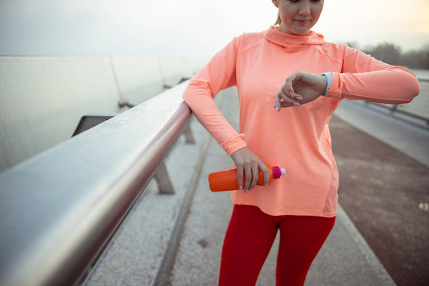 Sporty lady holding bottle of water and looking at her watch - Фото, зображення
