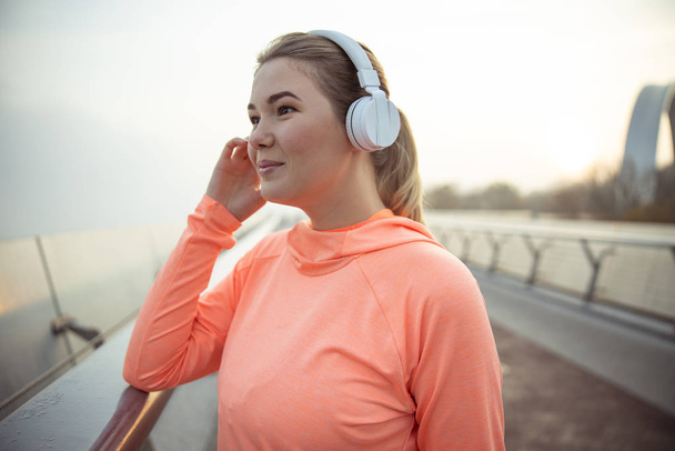Charming lady in wireless headphones standing on the street - Photo, Image