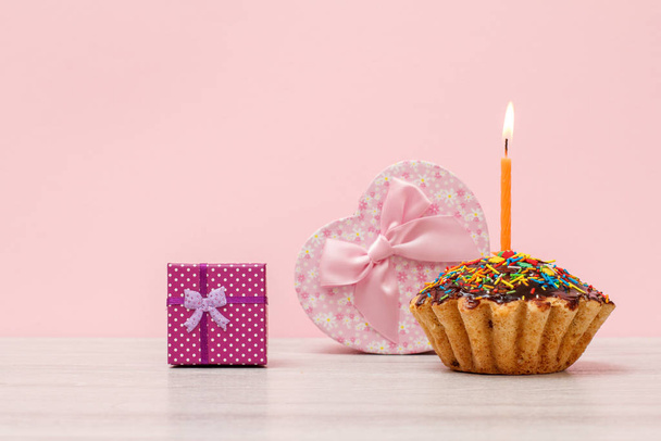 Birthday muffin with burning festive candle and gift boxes on the pink background. - Photo, Image