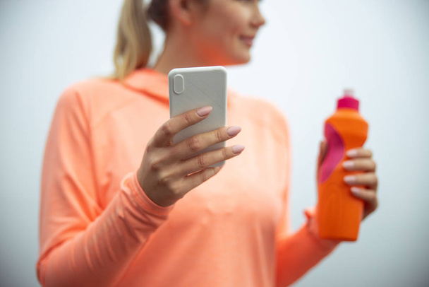 Young woman holding modern smartphone and bottle of water - Photo, Image