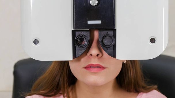 Офтальмологическое лечение - молодая женщина с ярко-розовыми губами, проверяющая остроту зрения специальным оптометрическим оборудованием
 - Фото, изображение