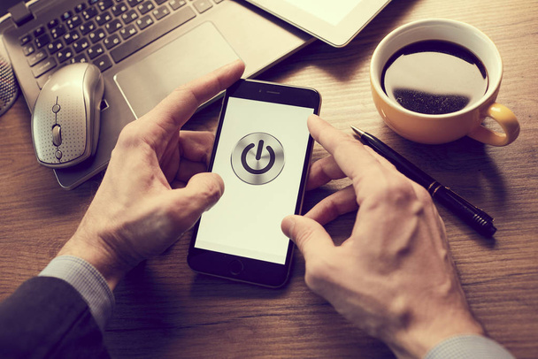 mannelijke handen houden moderne smartphone met power-knop op het scherm in het kantoor, business concept  - Foto, afbeelding
