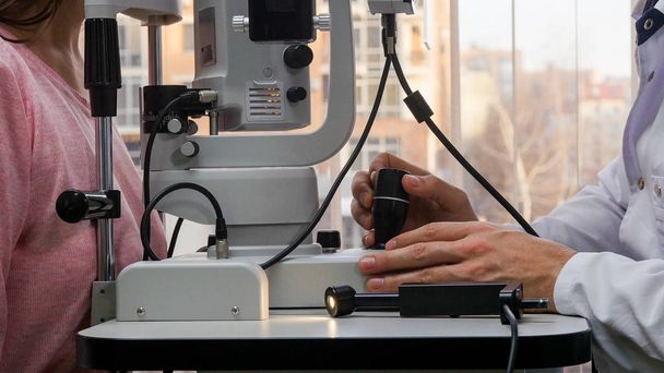 Οφθαλμολογική θεραπεία - ένας γιατρός που ελέγχει τις νεαρές γυναίκες οπτική οξύτητα με ένα ειδικό μηχάνημα σε ένα ευρύχωρο ντουλάπι - Φωτογραφία, εικόνα