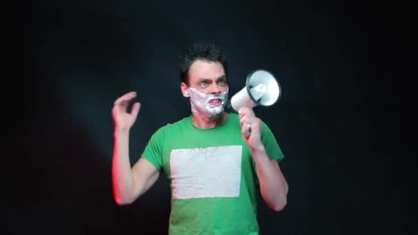 Angry man with shaving foam on his face shouting into a megaphone - Materiał filmowy, wideo