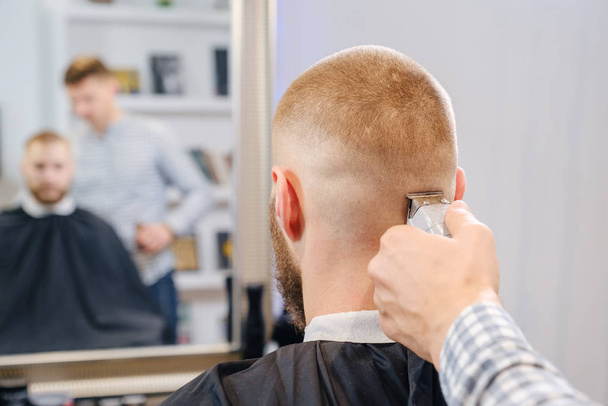 Il barbiere rasa la testa del cliente con un trimmer elettrico rosso. focus selettivo
 - Foto, immagini