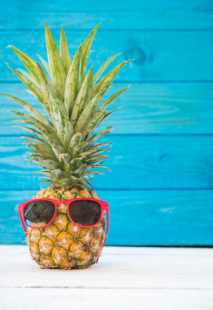 Holiday pineapple have sunglasses on blue wooden background, tropical holiday concept - 写真・画像