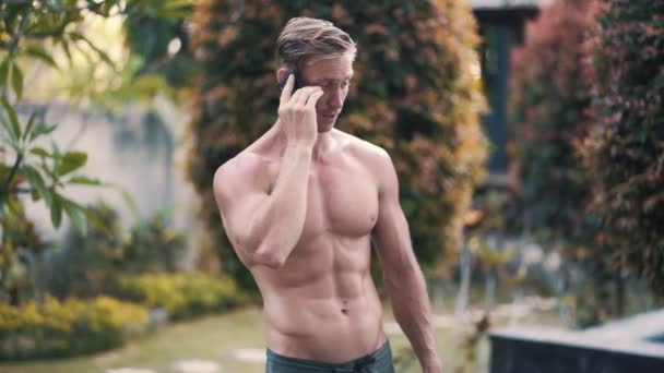 携帯電話の屋外で話している筋肉質の体を持つ白人男性,背景に緑 - 映像、動画