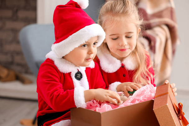 Lindos niños pequeños en trajes de Santa y con regalo de Navidad en casa
 - Foto, imagen