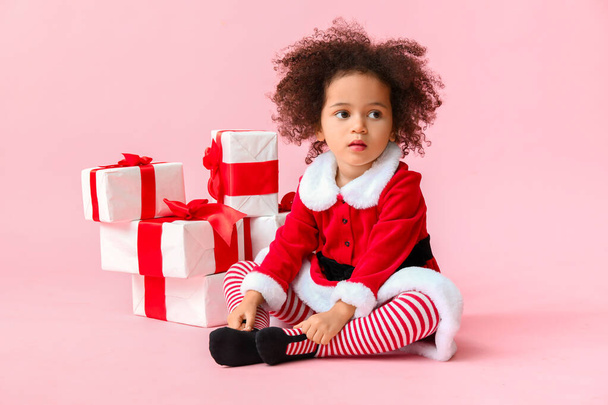 Klein Afrikaans-Amerikaans meisje in Santa kostuum en met geschenkdozen op kleur achtergrond - Foto, afbeelding