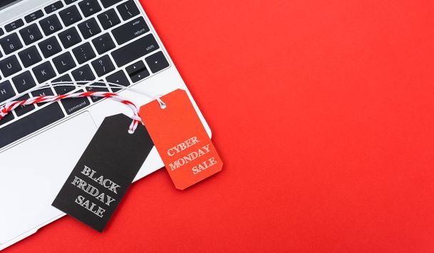 Internet online shopping marketing, top view of workspace with Black Friday text black tag and Cyber Monday text red tag near laptop computer on red background - 写真・画像