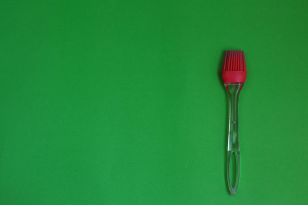 Червона кухонна силіконова щітка на зеленому фоні
 - Фото, зображення