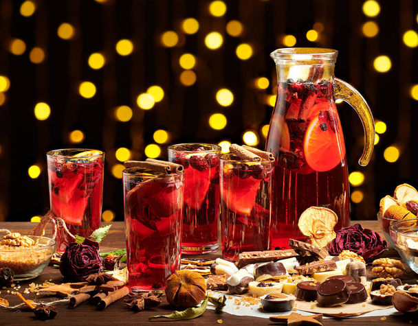 Christmas mulled wine or gluhwein with spices, chocolate sweets and orange slices on rustic table, traditional drink on winter holiday, christmas lights and decorations - Foto, afbeelding