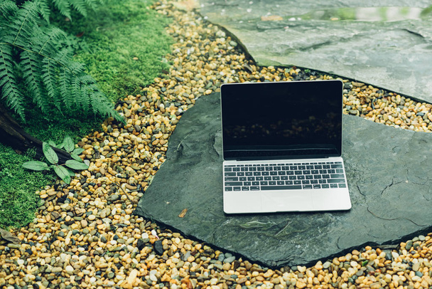 Computadora portátil mockup tiene pantalla vacía afuera en piedra en el jardín de la cafetería
. - Foto, imagen