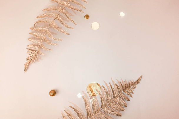 Festive composition. Shiny Christmas decorative floral fern branches, confetti, gold glitters on beige background. Flat lay. Copy space. Stylish christmas concept Minimalism - 写真・画像