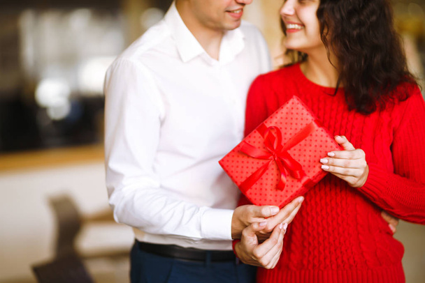 Woman with man holding a christmas gift in hand. Cheerful couple with gift in hands enjoying together on Christmas eve. Winter holidays concept. Lovers give each other gifts. Valentine's Day concept. - 写真・画像