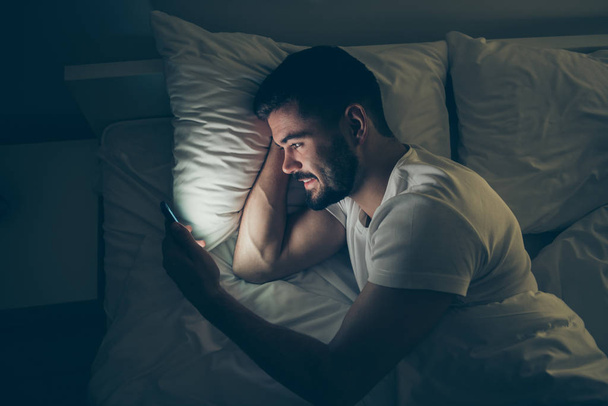 Top above high angle view portrait of his he nice attractive cheerful cheery guy lying in bed using digital cell chatting at night late evening home dark illuminated room flat house - Foto, Bild